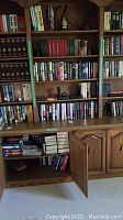 Bookshelves filled with an assortment of hardcover and paperback books, some open shelves with books stacked, wooden cabinetry below.