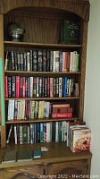 Wooden shelf filled with hardcover books in various genres including fiction and reference.