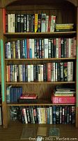 Wooden bookshelf with four shelves filled with hardcover and paperback books of assorted fiction and reference titles.