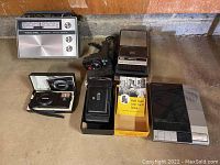 All items displayed together on concrete floor against wall, showing full set of cameras, radio, tape recorder, and telephone system.