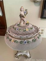 Porcelain Capodimonte soup tureen with lid, cherub figurine and floral decor, shown from front angle