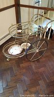 Front angled view of the brass and glass rolling tea cart showing two-tier design and contents on lower shelf.