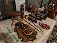 Overview photo showing all items on a white cloth including coat of arms plaque, swords, ashtray, stool, carved figure, and wall plaques.