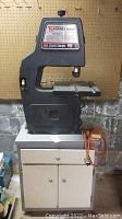 Full view of the Craftsman 10 inch band saw on a white cabinet stand in a basement setting.