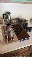 Photo showing insulated pourer, assorted cutlery, ornate stein, and glasses arranged on counter