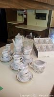 Full demitasse set with cups, saucers, coffee pot, creamer, sugar container arranged on a table