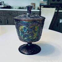 Front view of Fenton carnival glass pedestal bowl with lid showing iridescent, embossed grapevine and floral pattern.