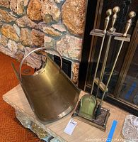 Brass fireplace tools and wood carriers arranged on stone hearth in front of fireplace.