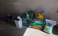 Photo of various garden supplies in bags and containers stacked against a wall, including MiracleGro and potting soil bags.
