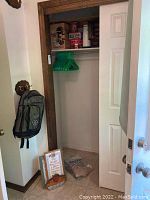 Closet area showing green hangers, some storage tins on shelf, a few packs on floor, and framed art leaning against wall near door.