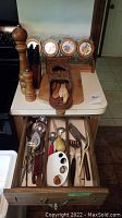 Wooden pepper grinder, glass canisters with holder, assorted metal utensils and cutlery in open drawer