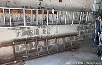 Image showing an aluminum extension ladder about 24 feet long and a wooden ladder about 12 feet long angled and leaning against a concrete block wall in a garage.