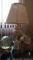 Photo of table lamp and four music boxes including two snow globes and figurine music boxes on glass tabletop