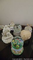 Photo showing all six music boxes grouped together on a surface, including angel figures, snow globes, and heart-shaped boxes.