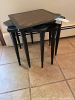 Stacked view of the set of three nesting tables showing black painted legs and inlaid wood square tops.