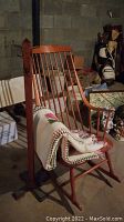 Wooden rocking chair with a handmade afghan draped over it and wooden coat rack behind