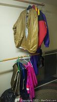 Hanging assorted ski clothing including gold synthetic jacket, color-block ski jacket, bright pink pants or outerwear, and other items.