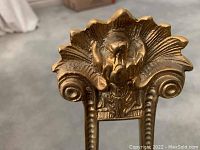 Close-up photo of the top detail of the brass easel showing floral and scroll design
