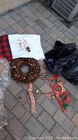 Image showing the natural pine cone wreath, a white fabric Christmas stocking with 'Holiday Cheer' text, 'Noel' wooden sign and some ornaments on a paved area.