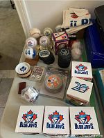 Collection of autographed baseballs, hockey pucks, coasters, fan towels, and sports memorabilia arranged on a white table.