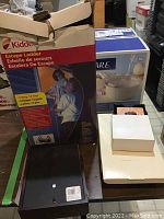 Overview of the sealed CorningWare box, Kidde escape ladder box, and coasters box on a table.