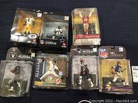 Overview of seven boxed sports figurines on black surface, six NFL McFarlane and one MLB