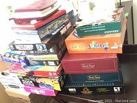 Stack of boxed board games with visible titles including Trivial Pursuit Junior, Checkers, and Floor Puzzle.