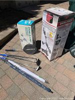 Photo showing Qwik-Fold golf cart box, Stow-A-Cart box, golf umbrellas, golf putters, and badminton racket on the ground.