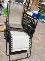 Front view of one folded gravity chair, showing beige fabric and rusted metal frame.