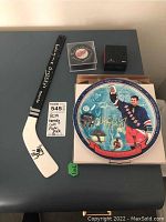 Overview of all items displayed: mini stick, commemorative plate in box, coin box, certificate, and puck
