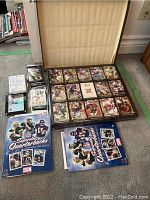 Photo showing opened 1991 Action Packed football card box with large NFL player cards arranged inside and assorted Topps cards and Toronto Sun NFL sticker albums on floor.