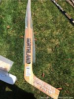 Full view of wooden Northland hockey stick lying on grass, showing branding and inscription area covered in plastic wrap.