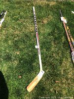 Full length of the KOHO hockey stick laid on grass, showing white shaft with branding and natural wood blade.