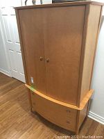 Front and angled views of the light wood modern wardrobe showing two doors and two drawers with metallic knobs, standing on tapered legs.