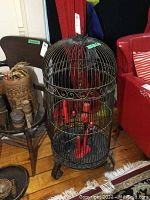 Front view of large metal bird cage with red candles inside showing rust and wear