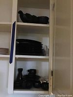 Shelf with stacked black ceramic plates, bowls, sake set, and serving tray visible on lower shelf