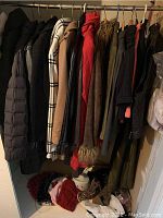 Full view of hanging women's winter clothing including jackets, wool coats, scarves, and hats on hangers and a mannequin head with hats below.