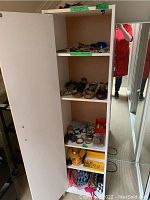 White cabinet shelves showing multiple jewelry items including bracelets, rings, pins, belt buckles, and pouches arranged on shelves.