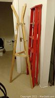 Photo of a natural wood coat tree and a red painted wood ladder standing side by side against a wall.