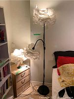 Wide view showing both lamps with matching crumpled white paper shades in lit condition, the floor lamp next to the bed and the table lamp on a small chest of drawers.