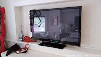 Front view of LG plasma TV showing screen and dark black bezel with cables coiled on top of the stand base on a white shelf.