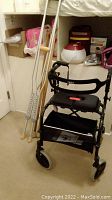 Nexus metal rollator walker with seat and storage bag alongside metal and wooden crutches, shelving with other items