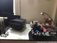 Photo showing various metal mesh office organizers: stackable trays, file holders, letter trays, and pen holders along with a variety of pens and desk items.