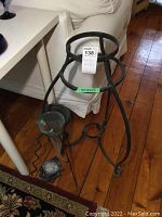 Black metal plant stand on wooden floor; three-legged curved base with circular top.
