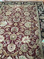 Full view of the floral patterned area rug showing the central red field with floral motifs and the black floral border, with visible stains and wear.