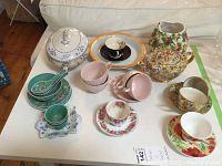 Overall view of several teacups, saucers, bowls, plates, teapot, and covered vegetable bowls arranged on white table