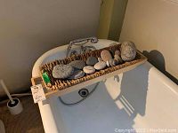 Wood and wicker tub shelf resting across bathtub with multiple smooth river rocks placed on top.