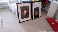 Two framed Rolling Stones tote bags featuring the iconic tongue and lips logo sitting on a carpeted floor.