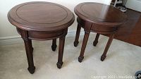 Photo showing both round wood accent tables side by side on carpet. Tables have dark polished wood, grooved top detail, four paneled legs with block feet.
