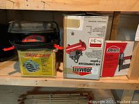 Shelf with boxed Job Mate air compressor and brad nailer, yellow Skil circular saw case, Black & Decker sander on shelf